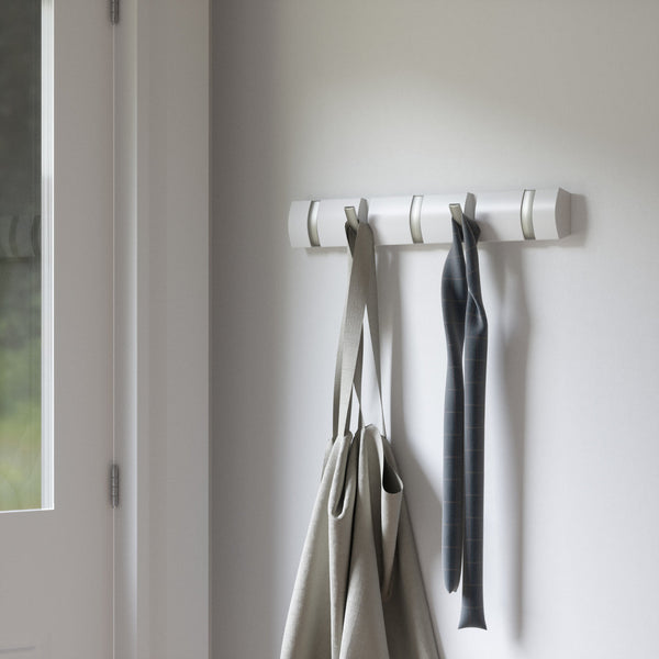 A Umbra Flip 5 Hook White wall mounted coat rack with a bag hanging on it, providing space-saving functionality.