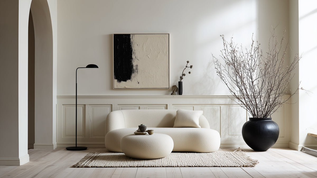 Airy monochrome living room with cream bouclé sofa, black floor lamp, large black-on-linen artwork, and an oversized black urn of bare branches.