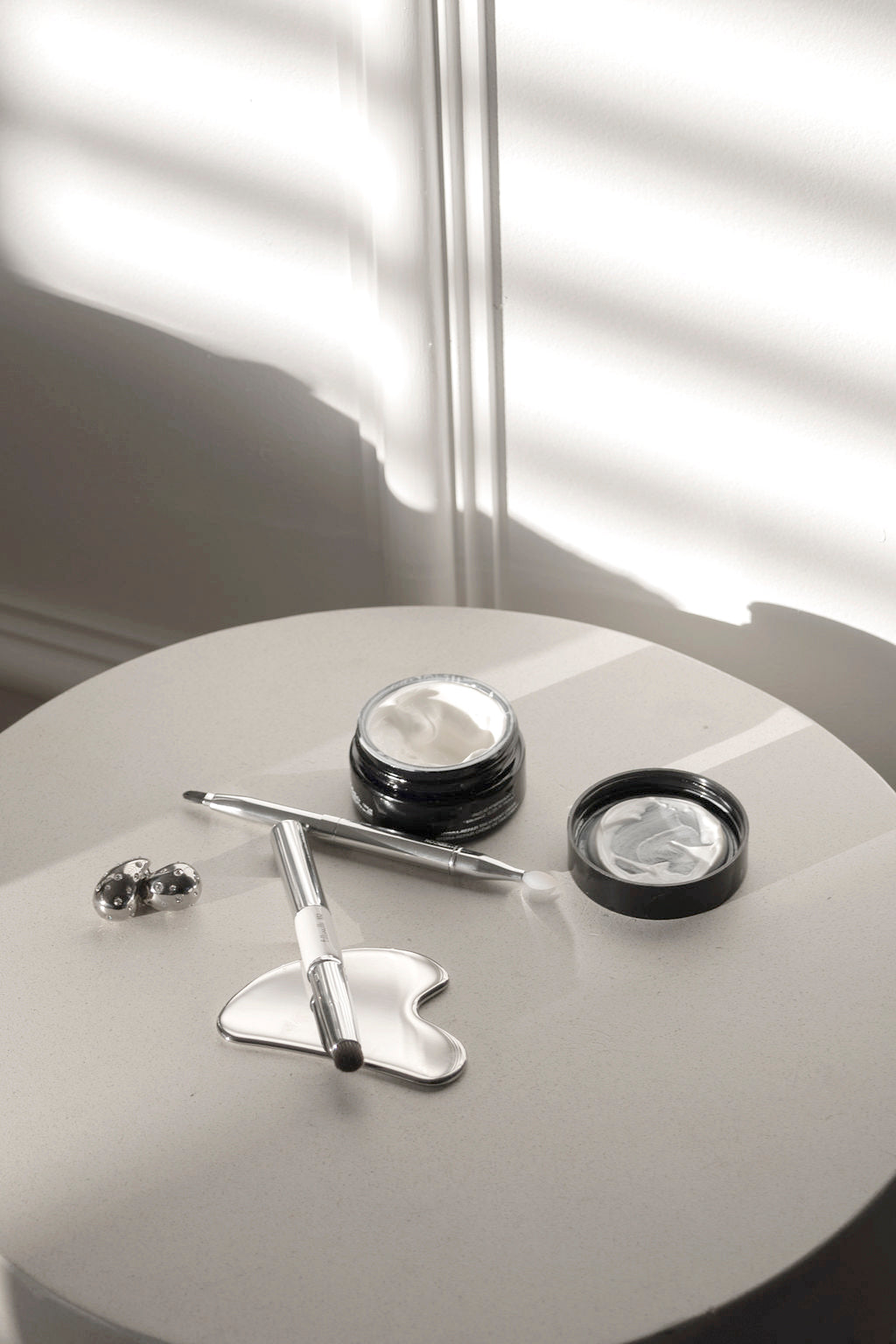 Round table holding jewellery dishes and a pen in striped window light