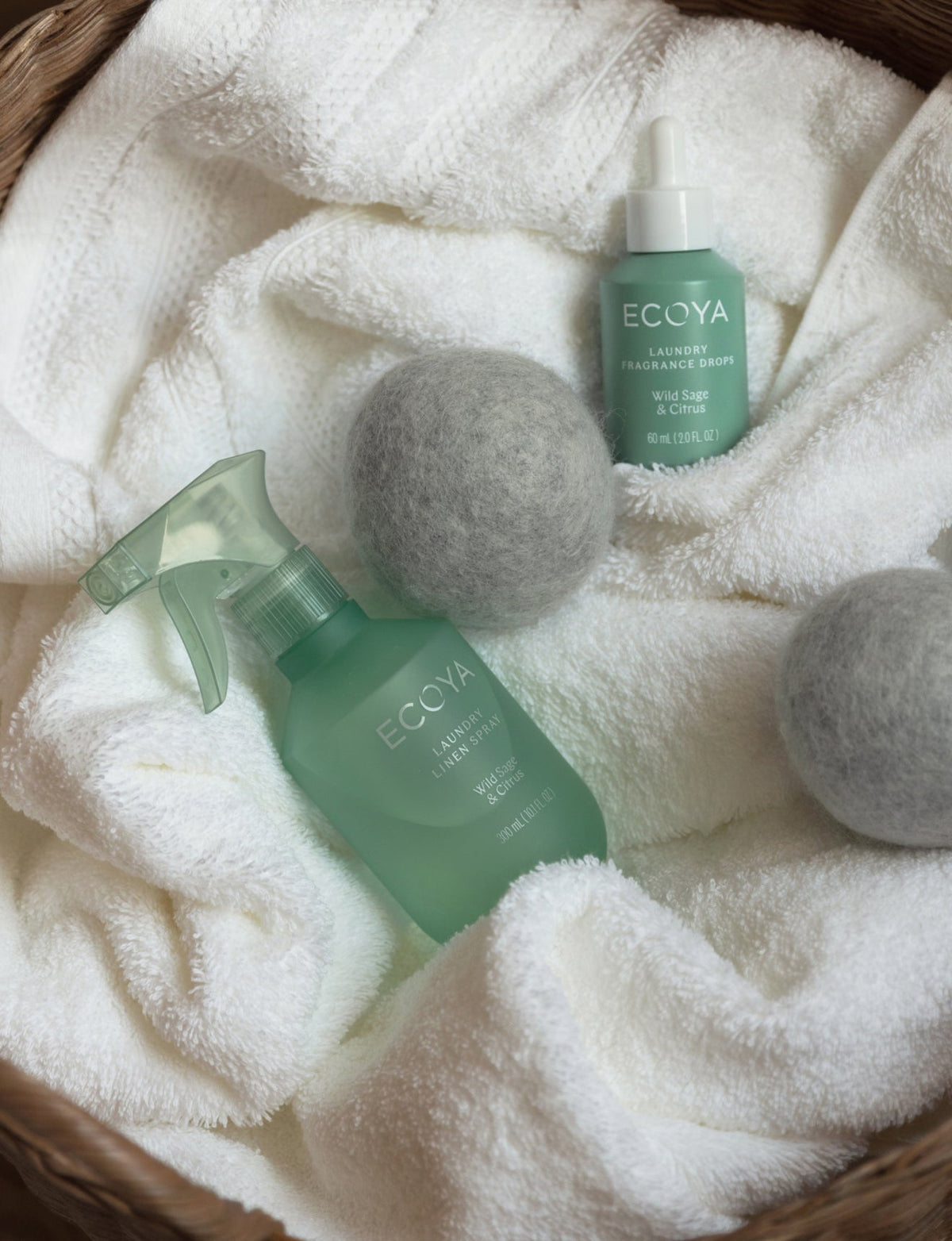 Ecoya Wild Sage and Citrus linen spray, laundry fragrance drops and wool dryer balls in a basket of white towels