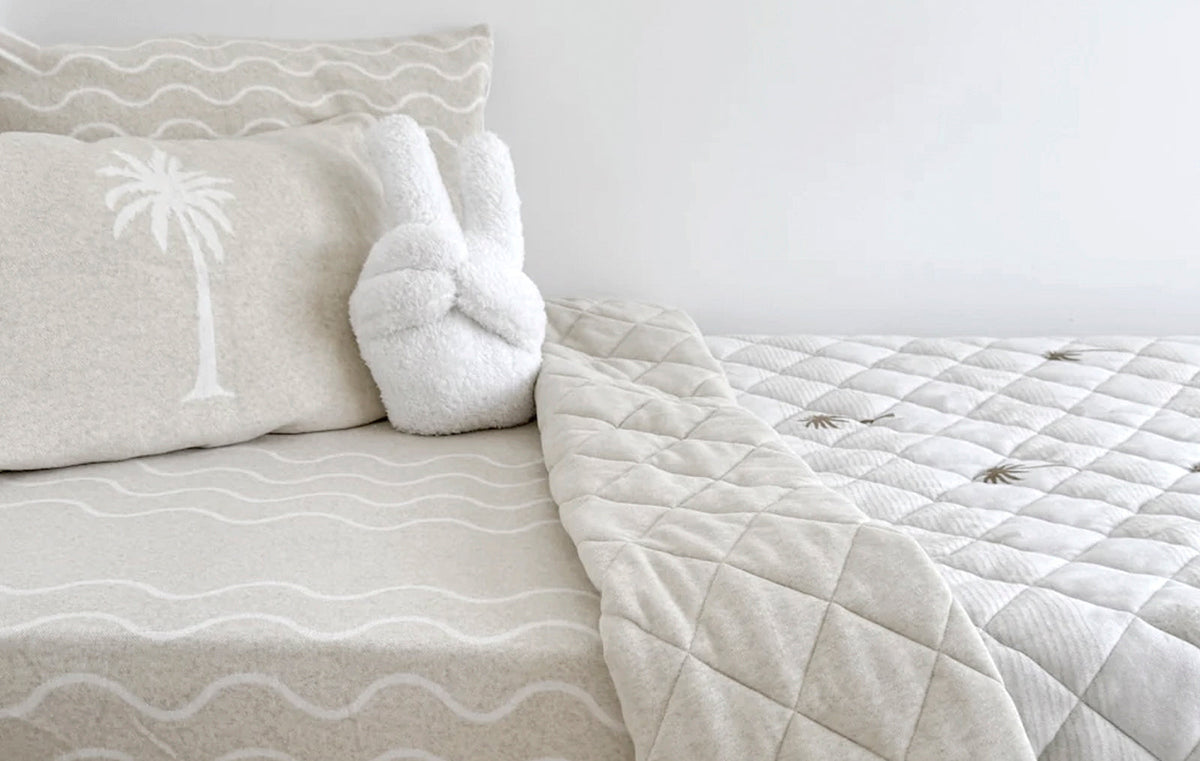 Neutral kids’ bedding with palm tree print, wave pattern sheets, and a plush peace-sign cushion
