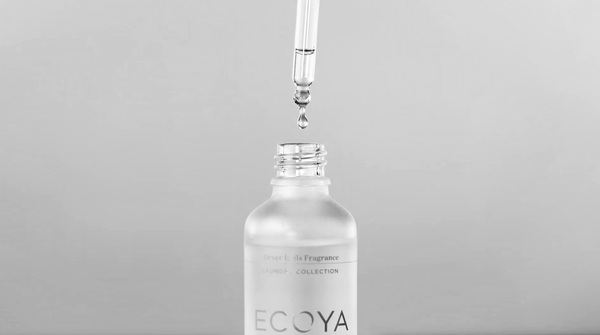 A close-up of a dropper releasing a droplet into a frosted ECOYA bottle, capturing a sense of purity, care, and elevated everyday rituals.