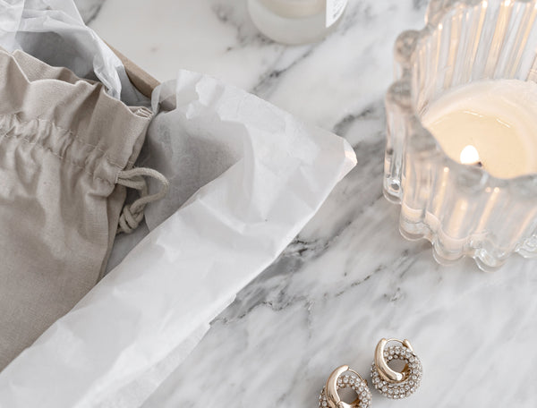 Marble tabletop scene styled with a natural linen pouch, delicate gold and crystal earrings, and a sculptural glass candle, capturing the understated elegance and tactile softness at the heart of quiet, grounded luxury.