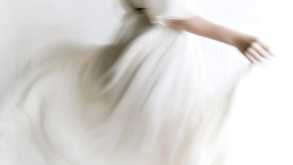 Abstract motion blur of a flowing white dress and outstretched arm, symbolising energy, movement, and aligned intention — a visual metaphor for manifestation and flow state.