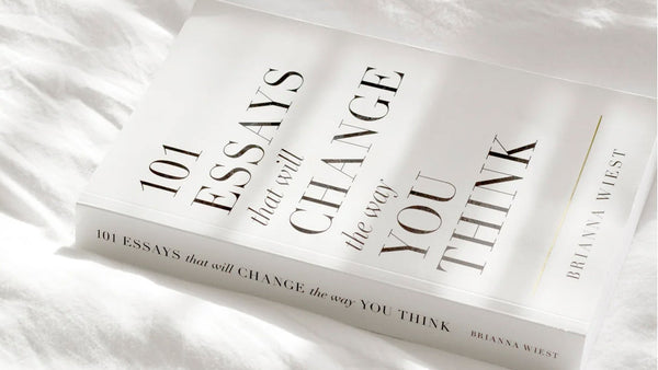 Flatlay of the book “101 Essays That Will Change the Way You Think” by Brianna Wiest, resting on soft white bedding in natural light—evoking calm, clarity, and introspection.