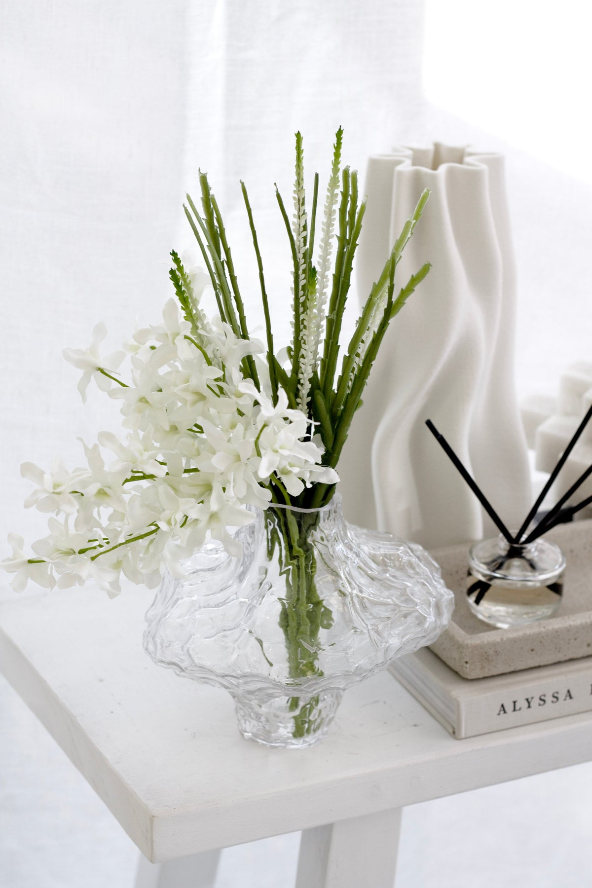 White faux orchids in a textured glass bowl on a white table