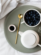 A tray with blueberries and a Zakkia handmade brass teapot on a bed.