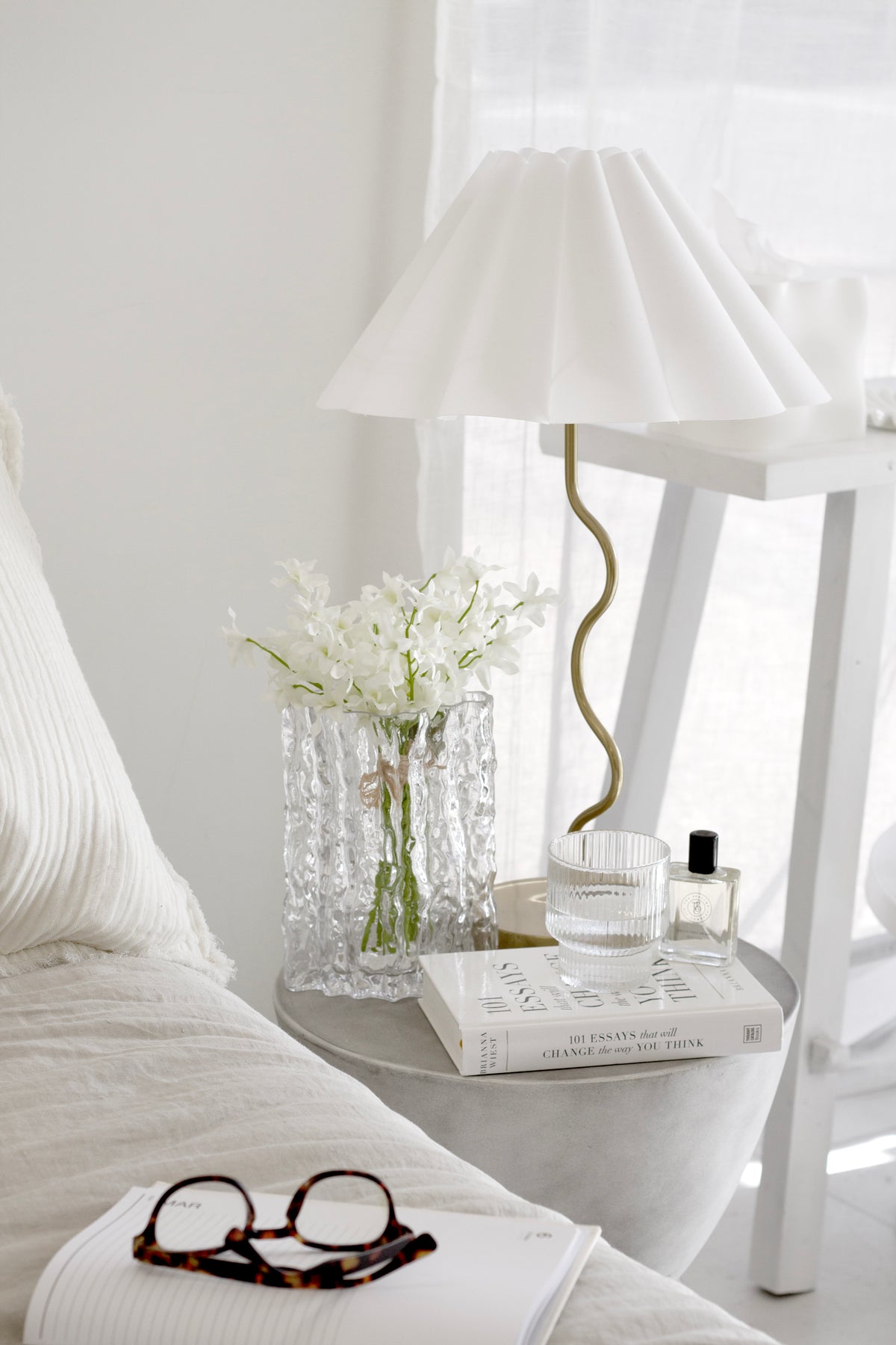 101 Essays That Will Change The Way You Think book styled on a bedside table with flowers, lamp, and glass of water