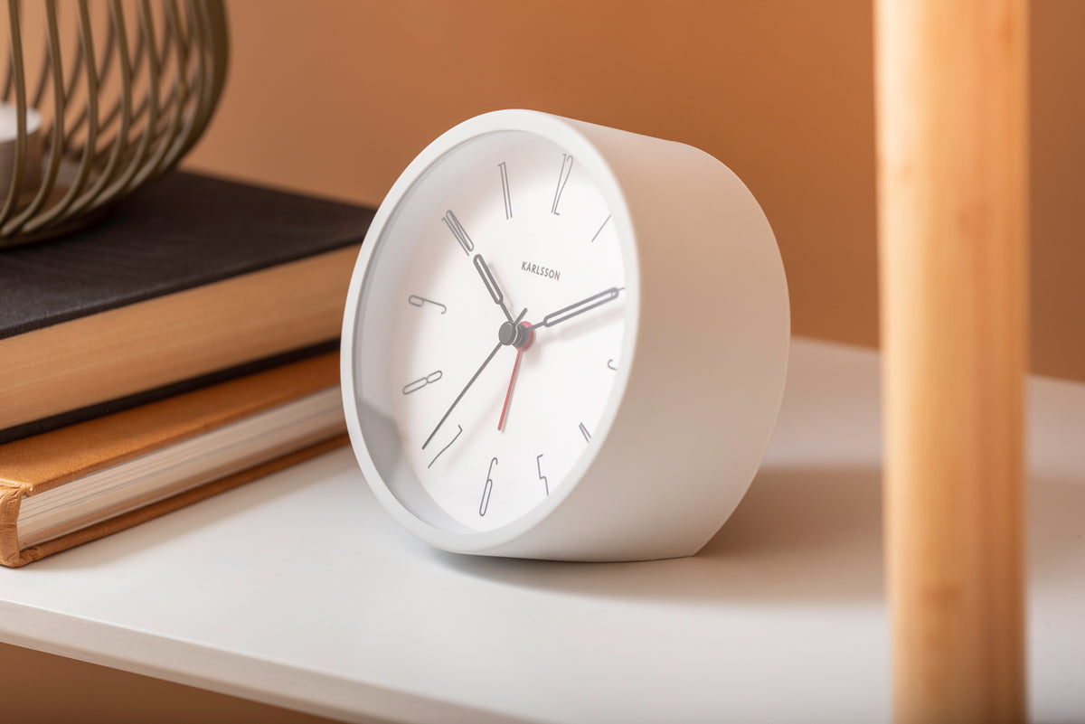 White Belle alarm clock on a white shelf with books against a terracotta wall