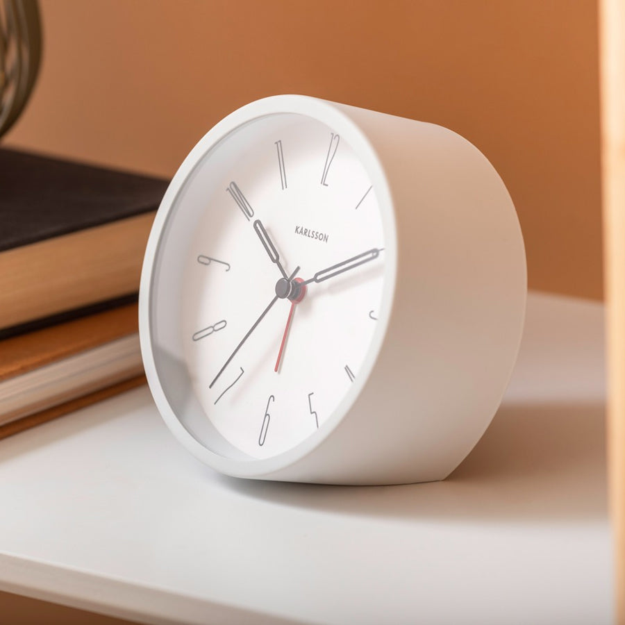 White Belle alarm clock on a white shelf with books against a terracotta wall