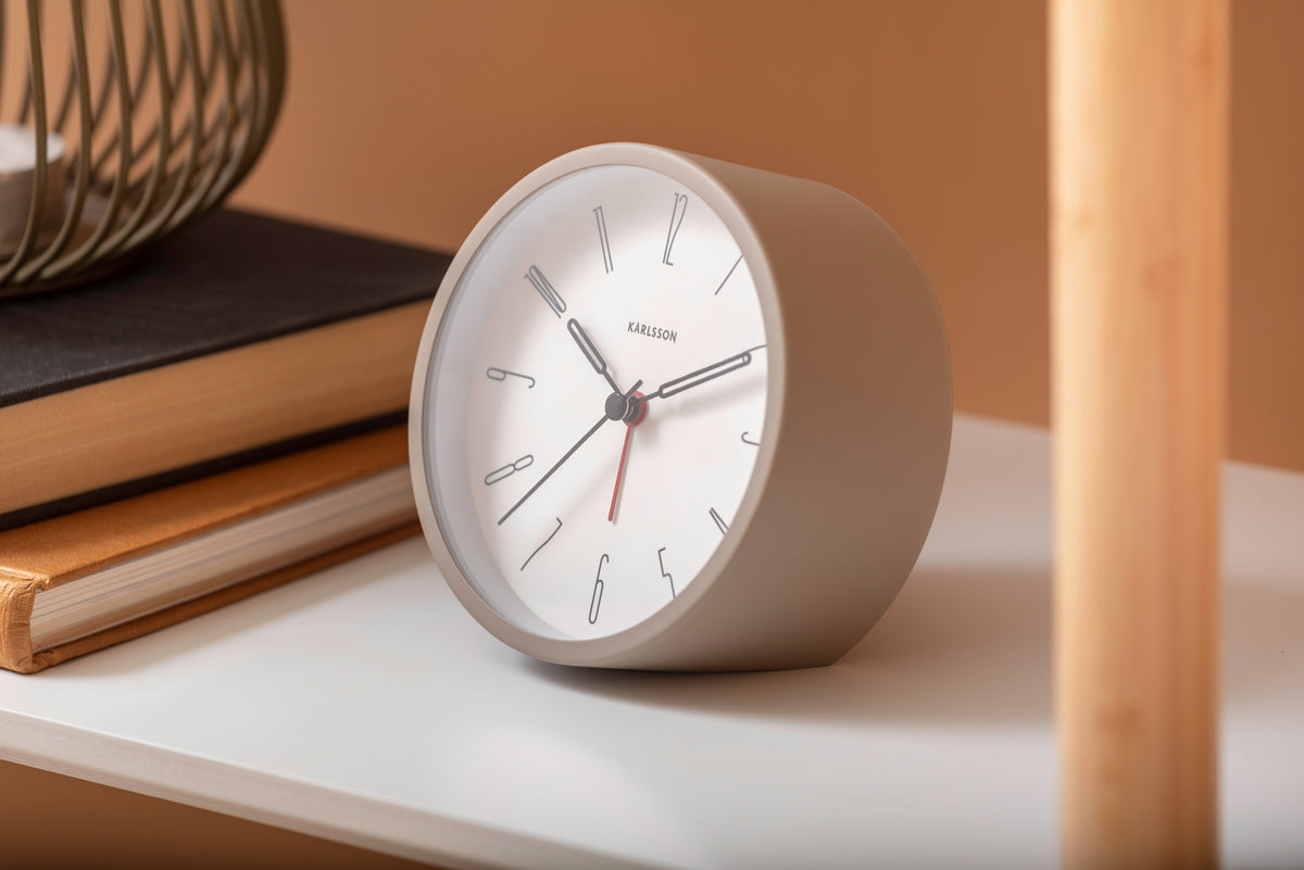 Grey Belle alarm clock on a white shelf with books against a terracotta wall