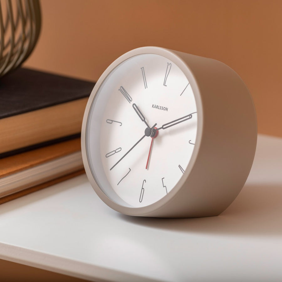 Grey Belle alarm clock on a white shelf with books against a terracotta wall