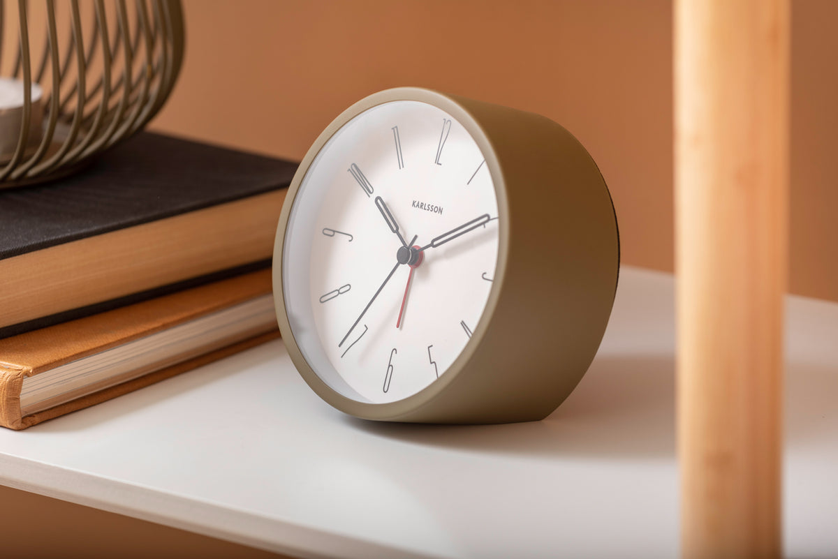 Moss Green Belle alarm clock on a white shelf with books against a terracotta wall