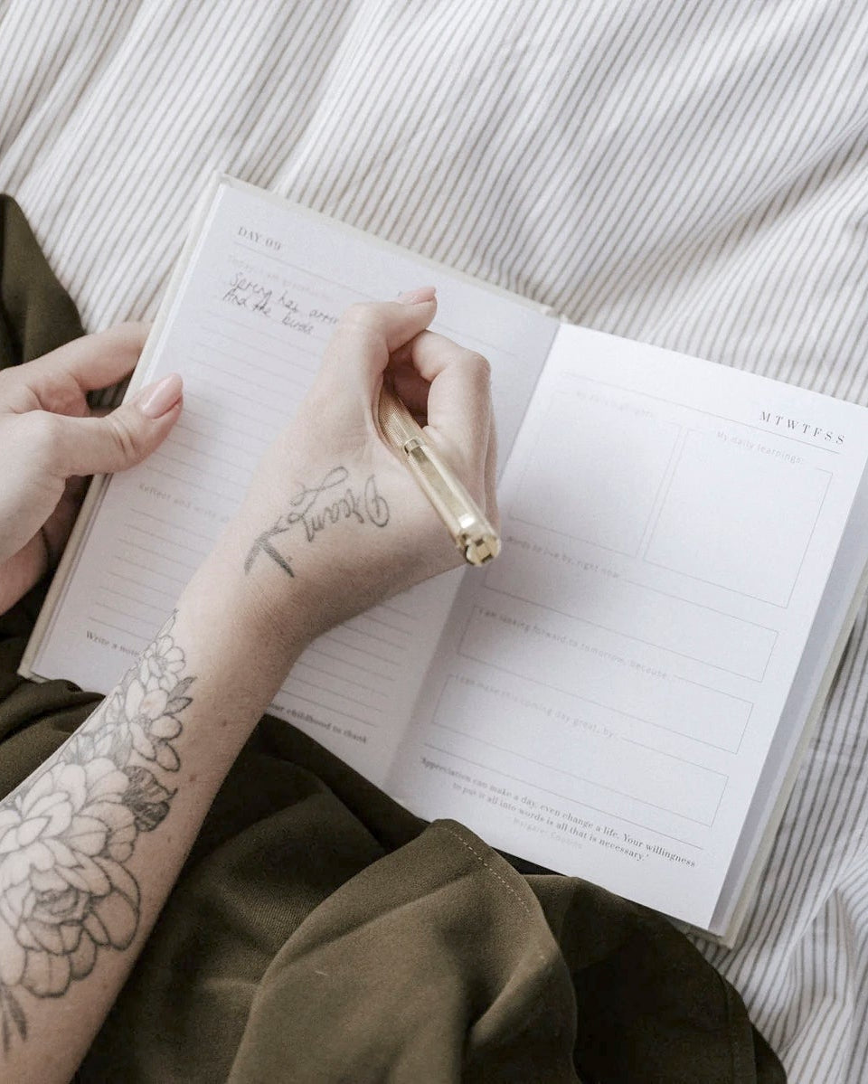 Hands writing in the open One Hundred Days of Gratitude journal