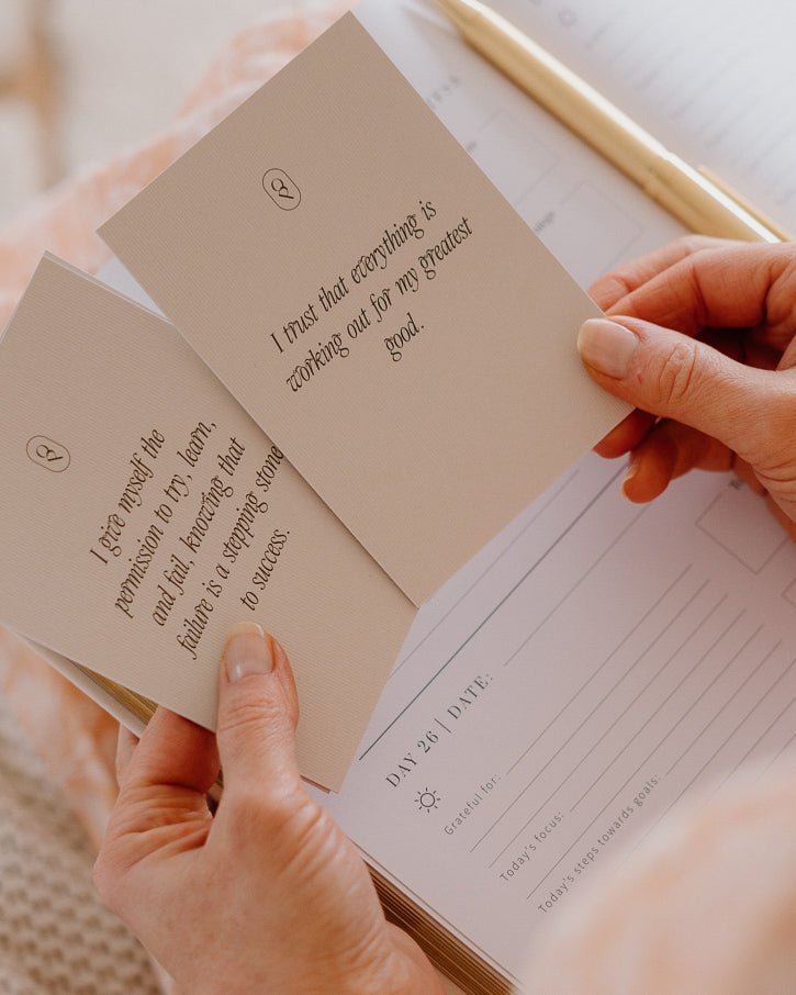 Hands holding an affirmation card over an open journal