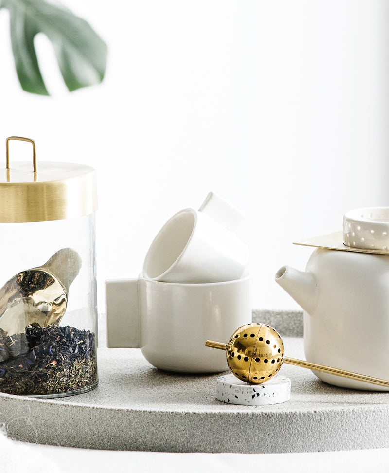 A white teapot and a gold teapot are elegantly displayed on a Zakkia Terrazzo Dimple Tray - Small Snow, accentuated with terrazzo chips.