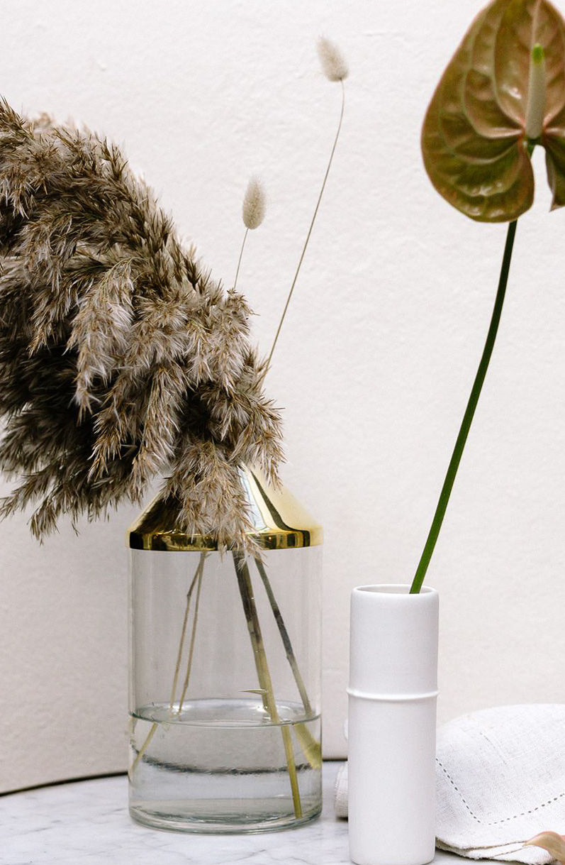 A Botanical Vase - Large Brass by Zakkia with a plant and a handmade book on a table.