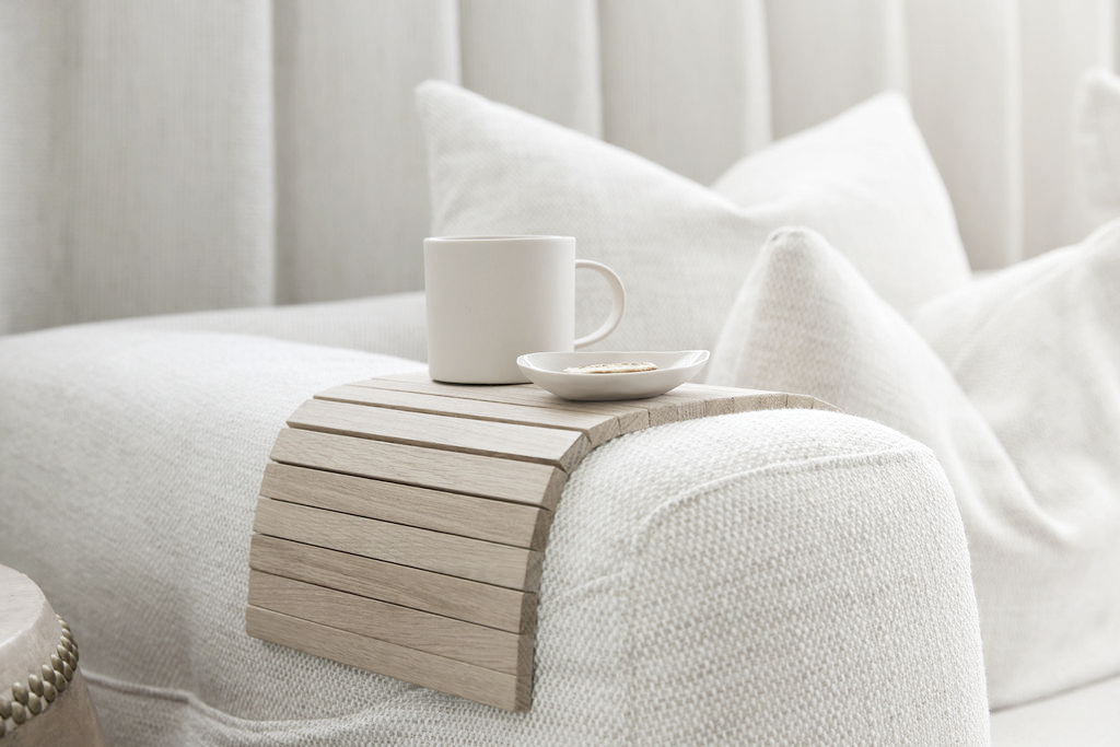 Oak slatted armchair tray draped over the arm of a white sofa holding a mug and saucer