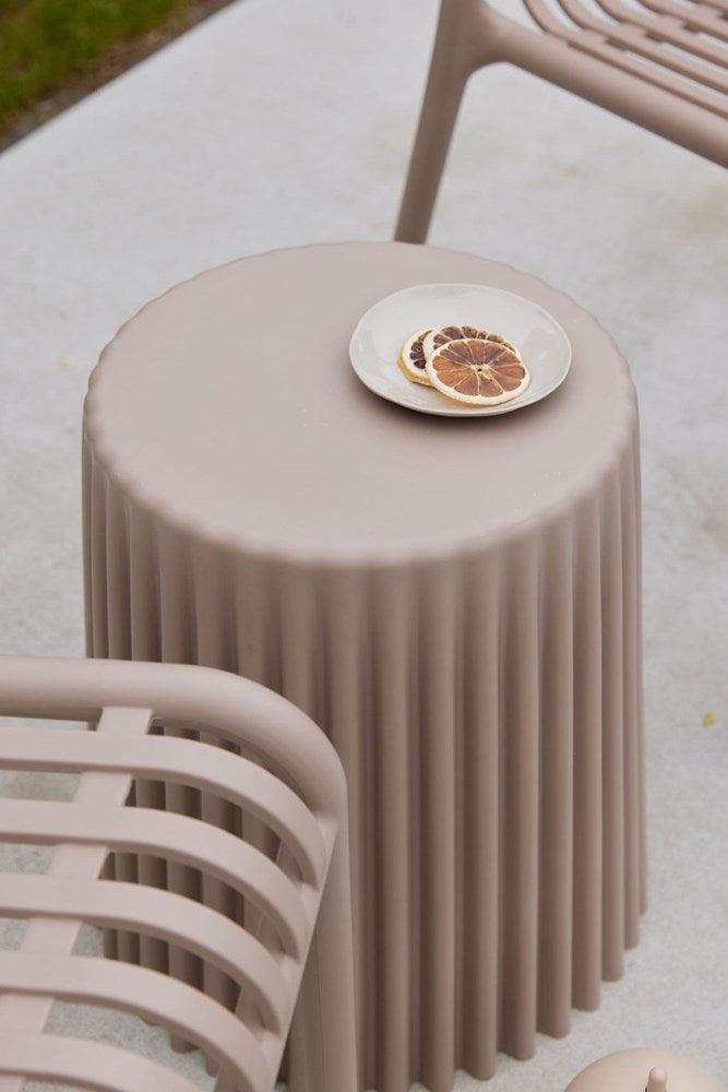 Nude ribbed stool on paving holding a plate of dried citrus slices beside a matching outdoor chair