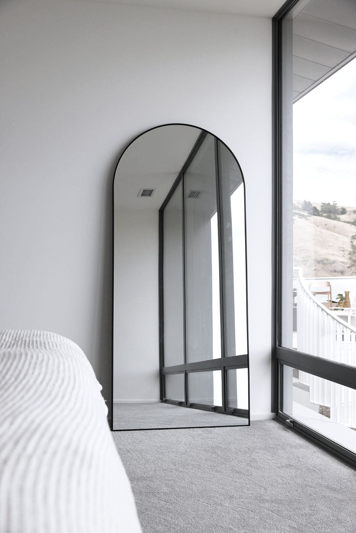 Arch floor mirror leaning against a bedroom wall