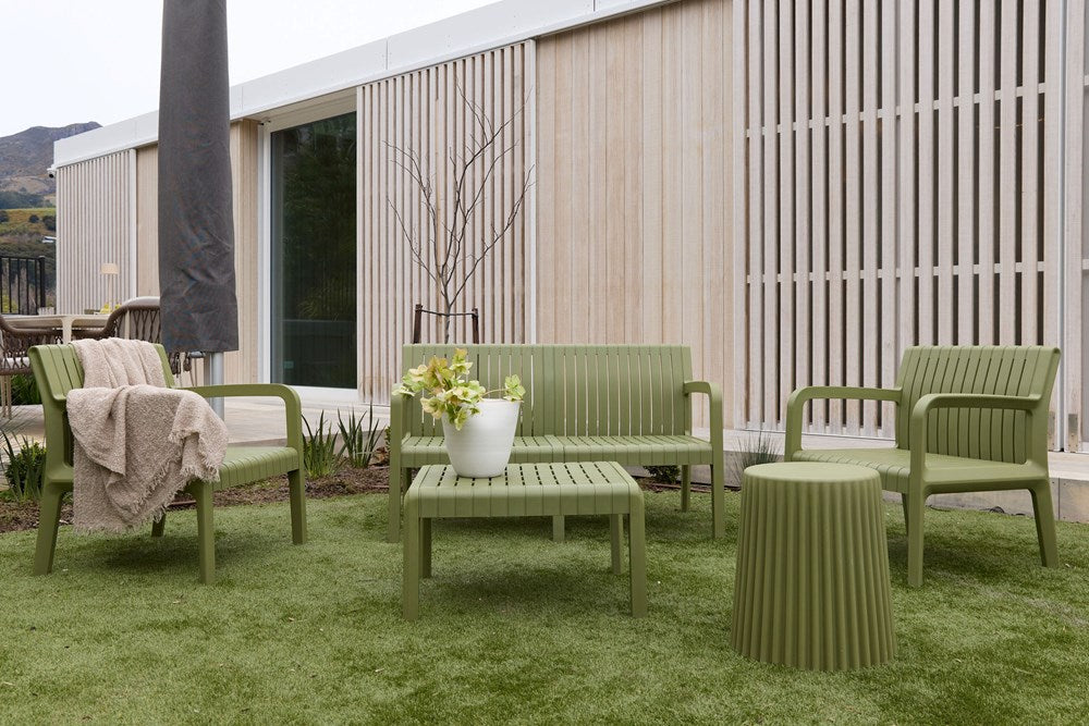 Olive ribbed stool used as a side table beside outdoor seating on grass by a timber clad house