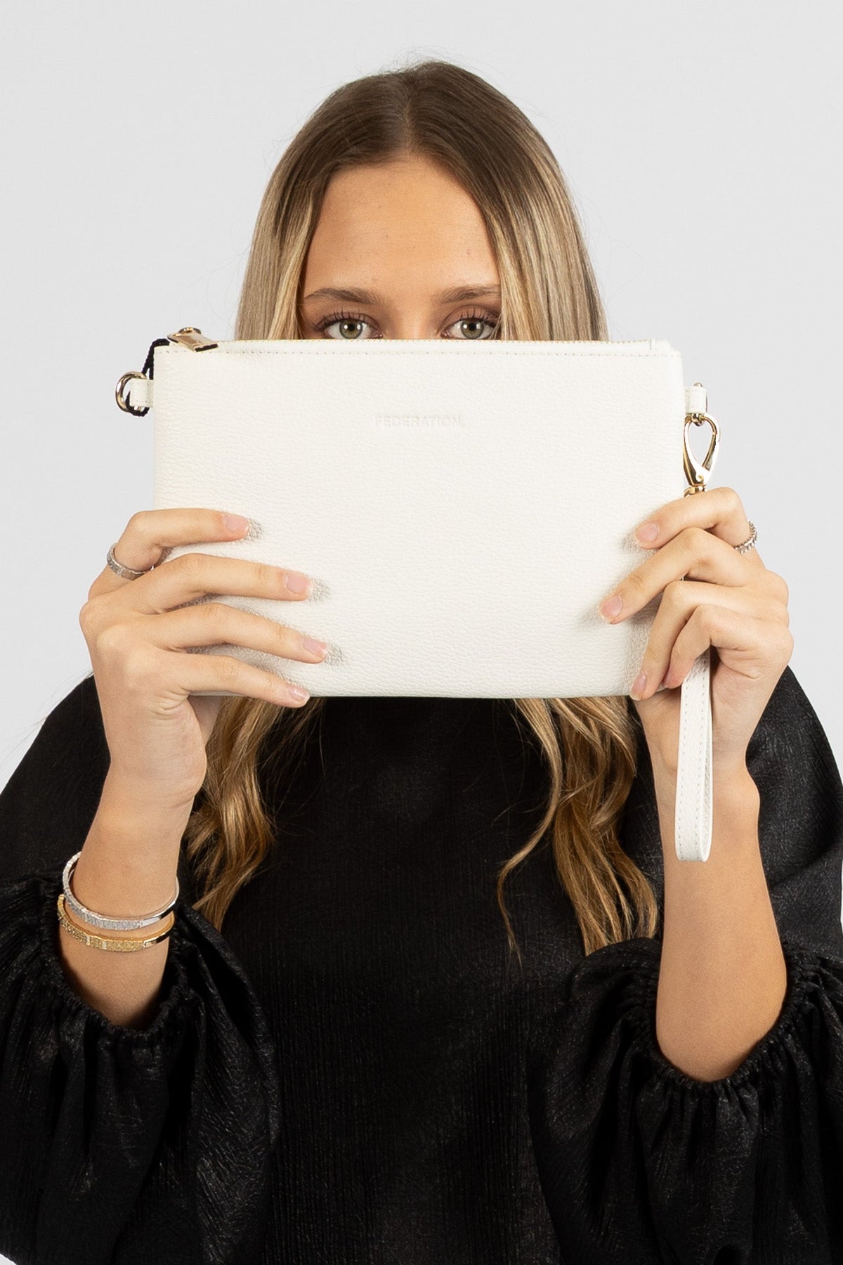 Model holding the white Ryder leather bag as a clutch, showing the pebbled leather and gold clips