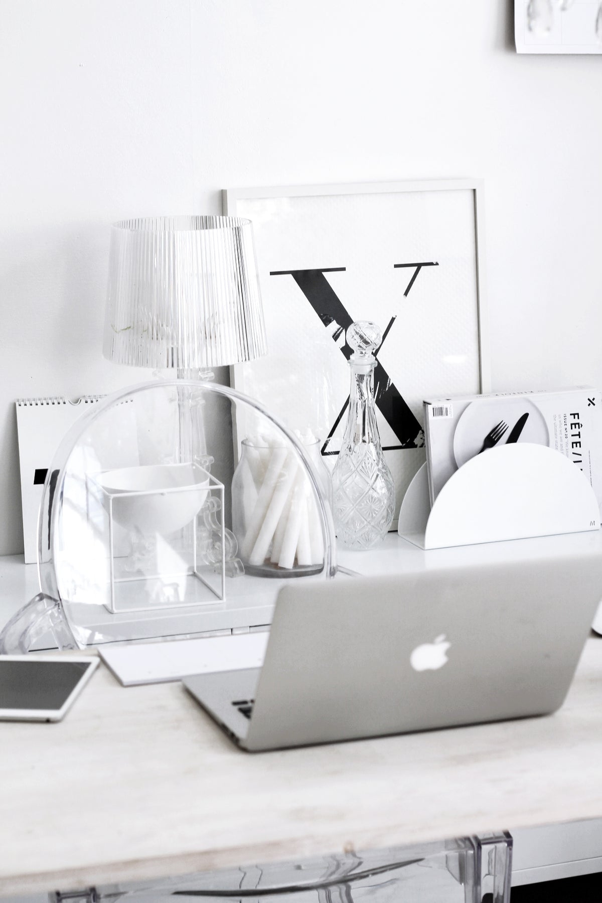 Clear acrylic chair at a white desk with a ribbed lamp, framed letter print and a laptop