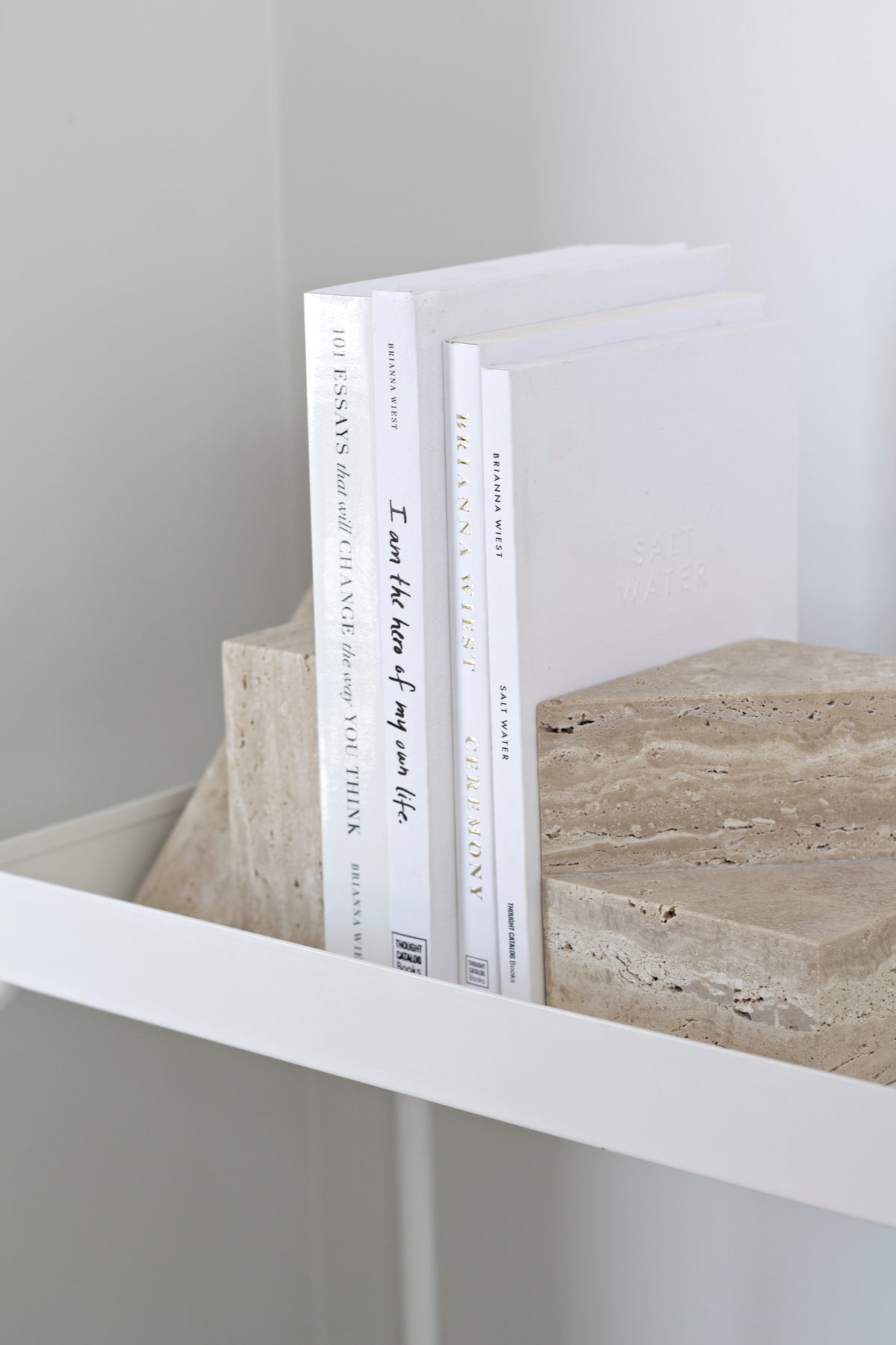 Travertine bookends holding white spined books upright on a white shelf