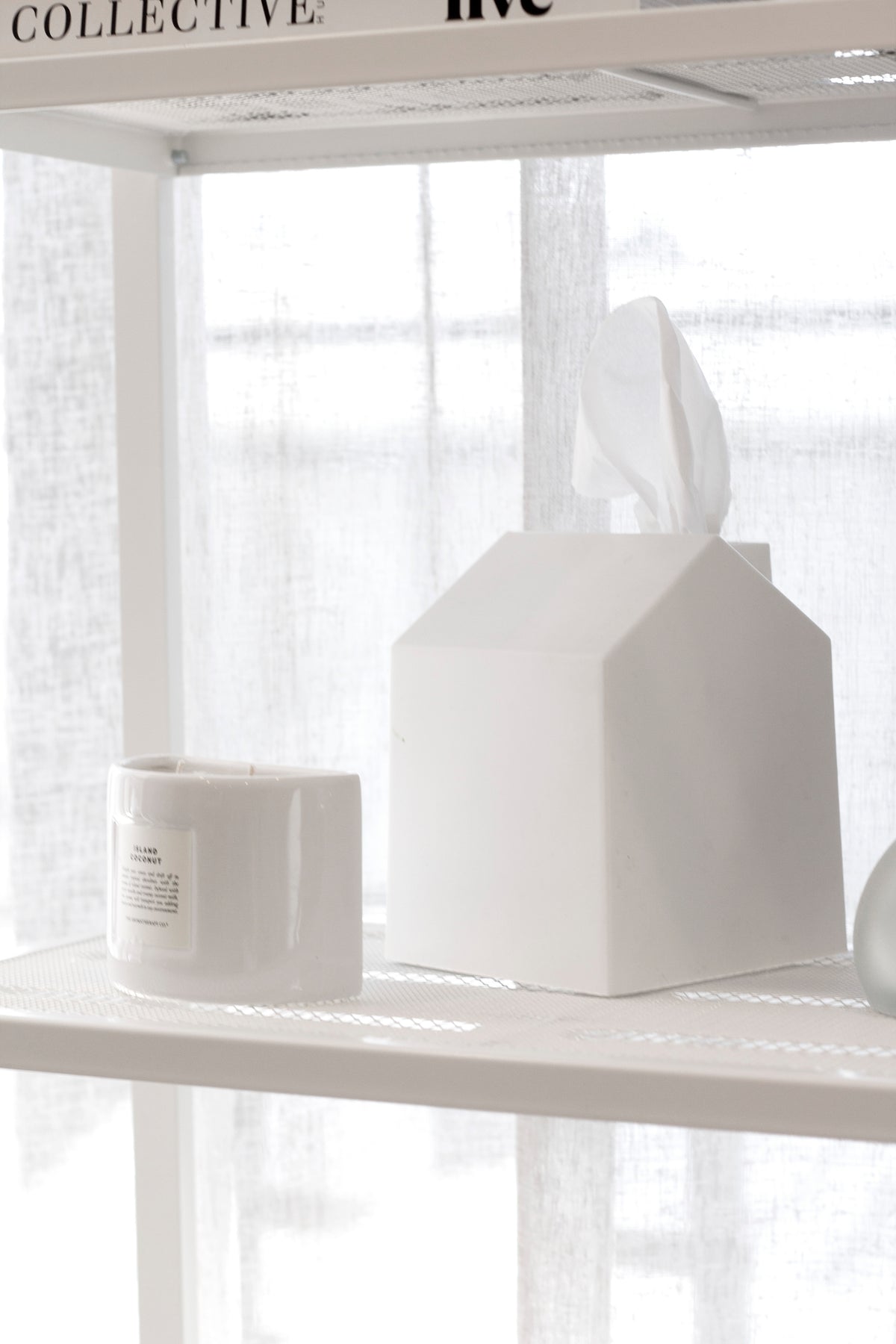 Umbra Casa white house-shaped tissue box cover on a shelf beside a candle and sheer curtain
