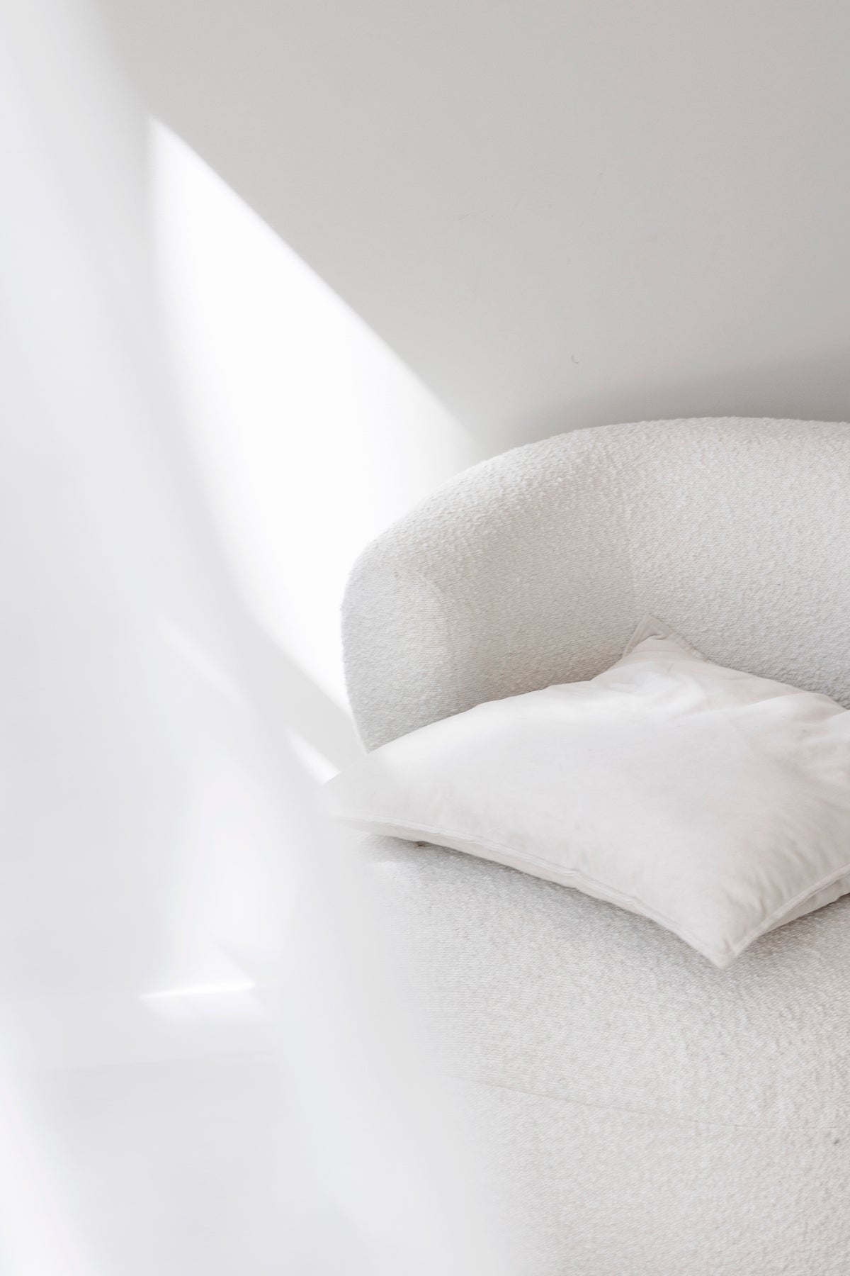 Boucle armchair with a cushion, side light raking across the wall behind