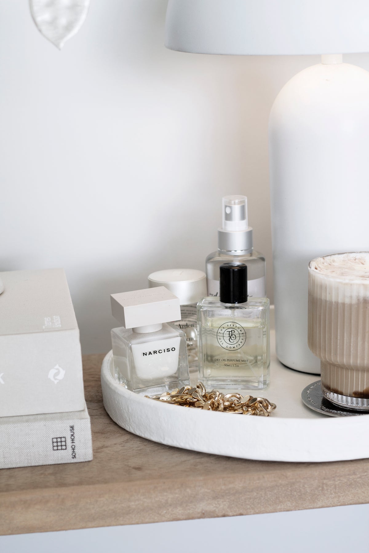 Perfume oil bottles on a round tray beside a lamp and vase on a timber surface
