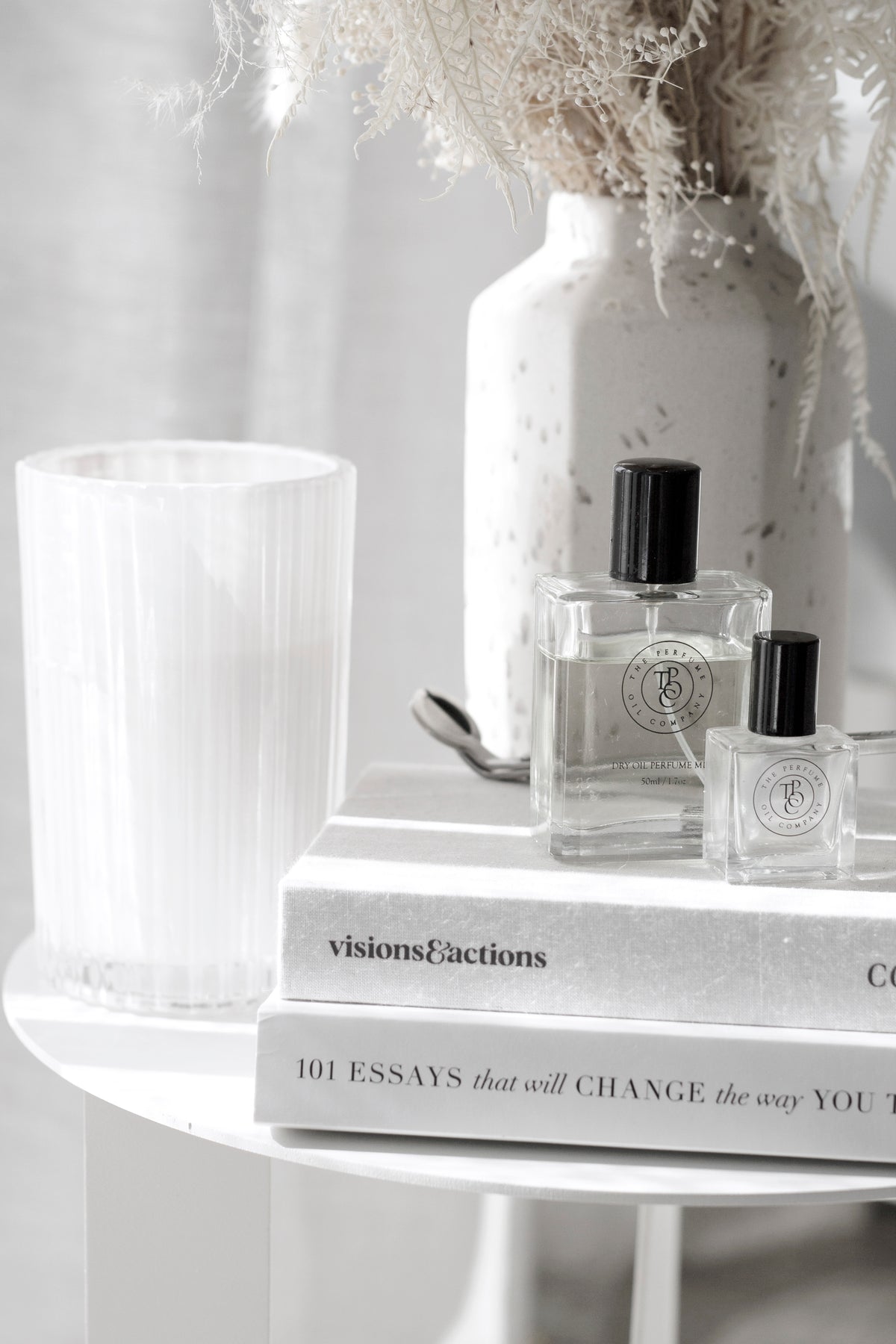 Perfume oil bottles on a white shelf with a vase and books in soft light