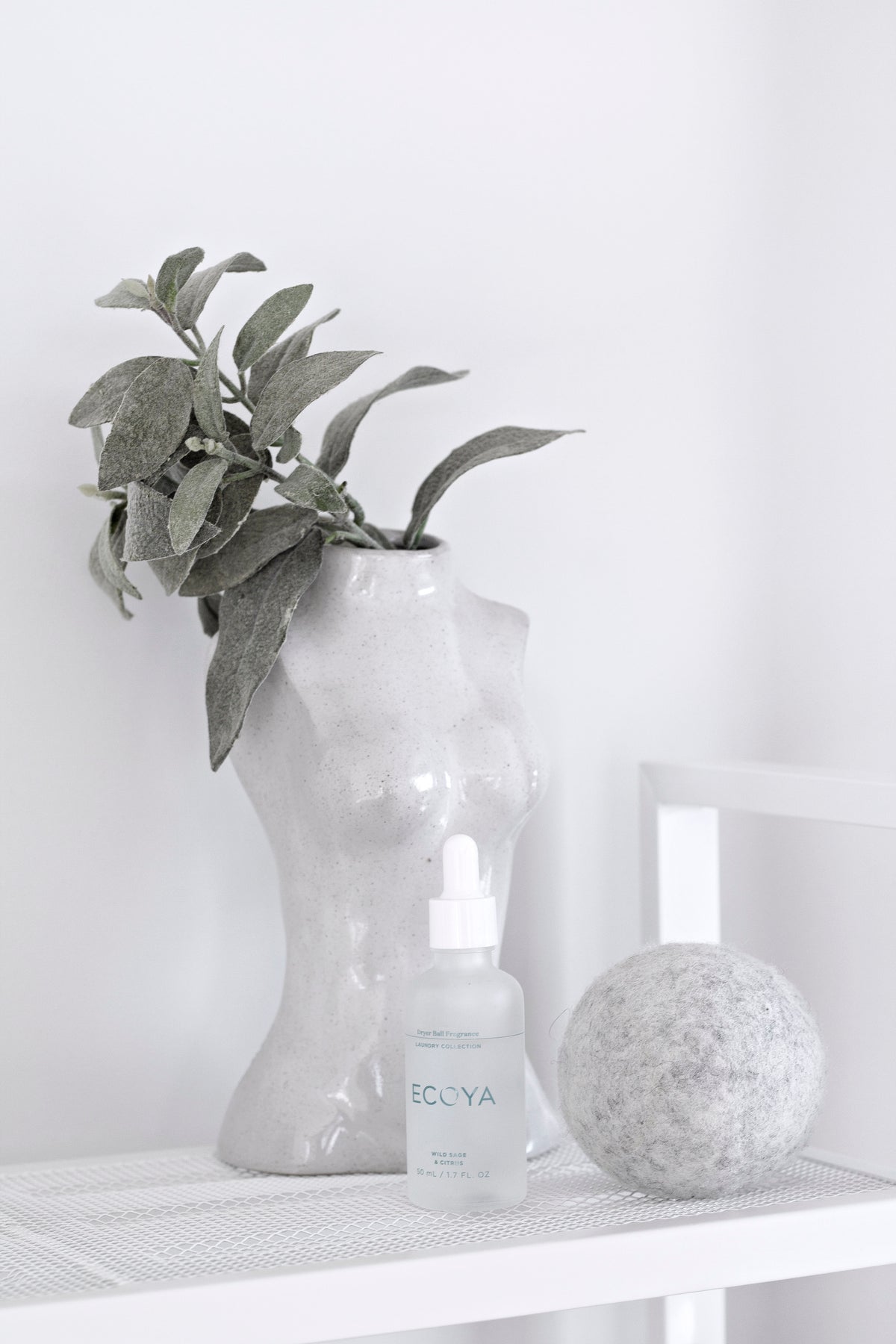 Female Silhouette Vase holding green foliage on a white shelf beside a glass bottle and stone ball