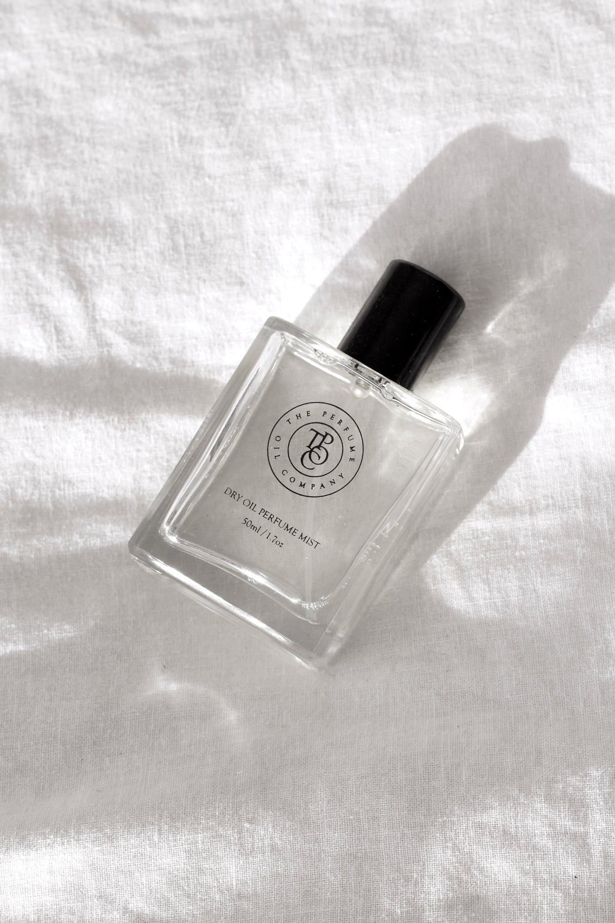 Perfume oil bottle resting on sunlit white linen with soft shadows