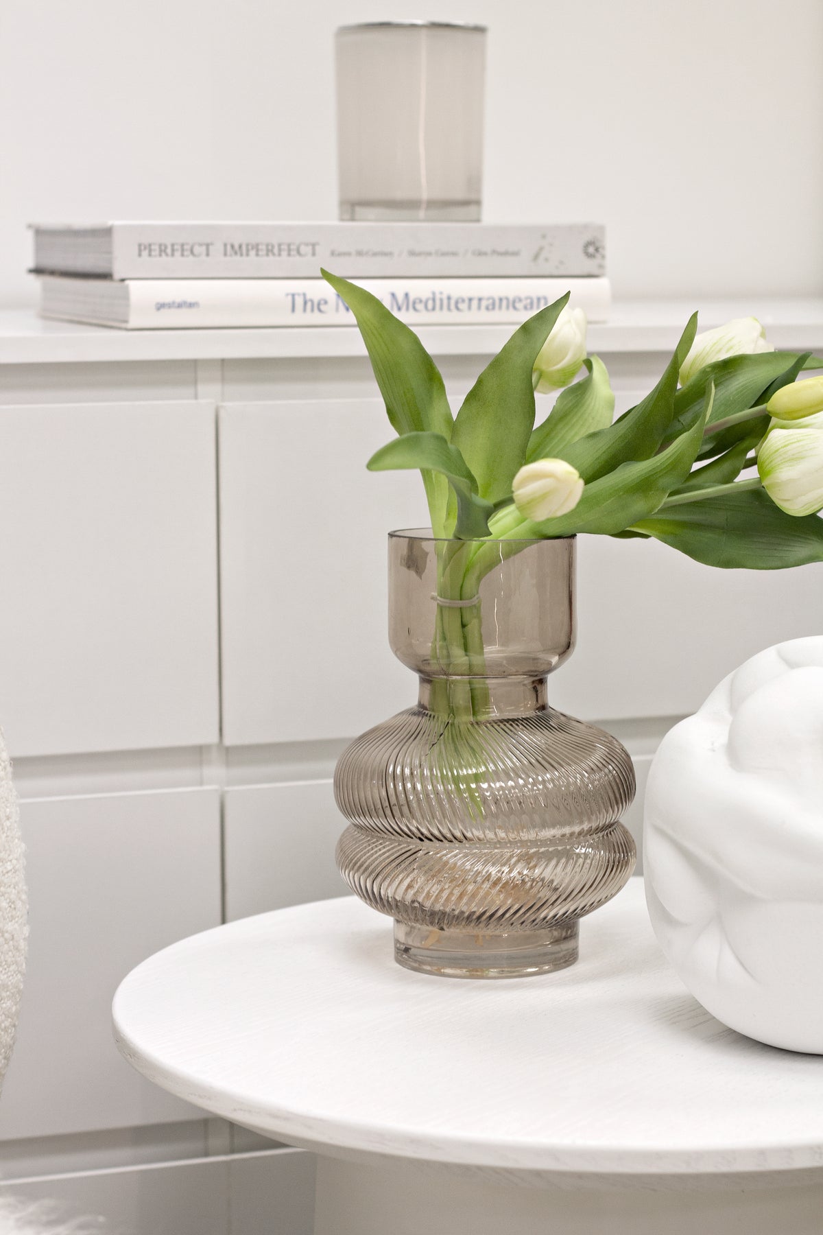 White Strato Side Table styled with a ribbed glass vase of white tulips beside a white cabinet