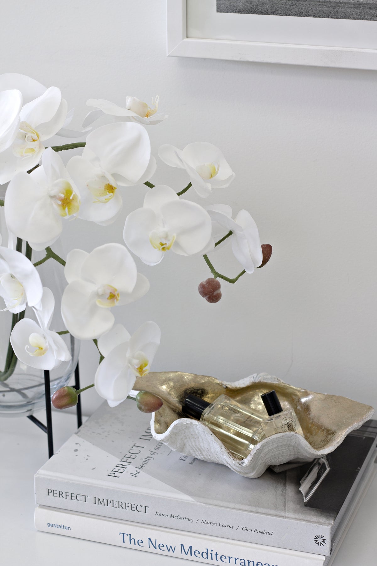 Clam shell bowl on a stack of white books beside a white orchid in a bright room