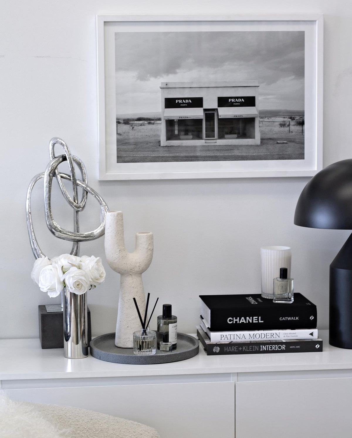 Small Franki vase on a white sideboard with a framed print, lamp and vases