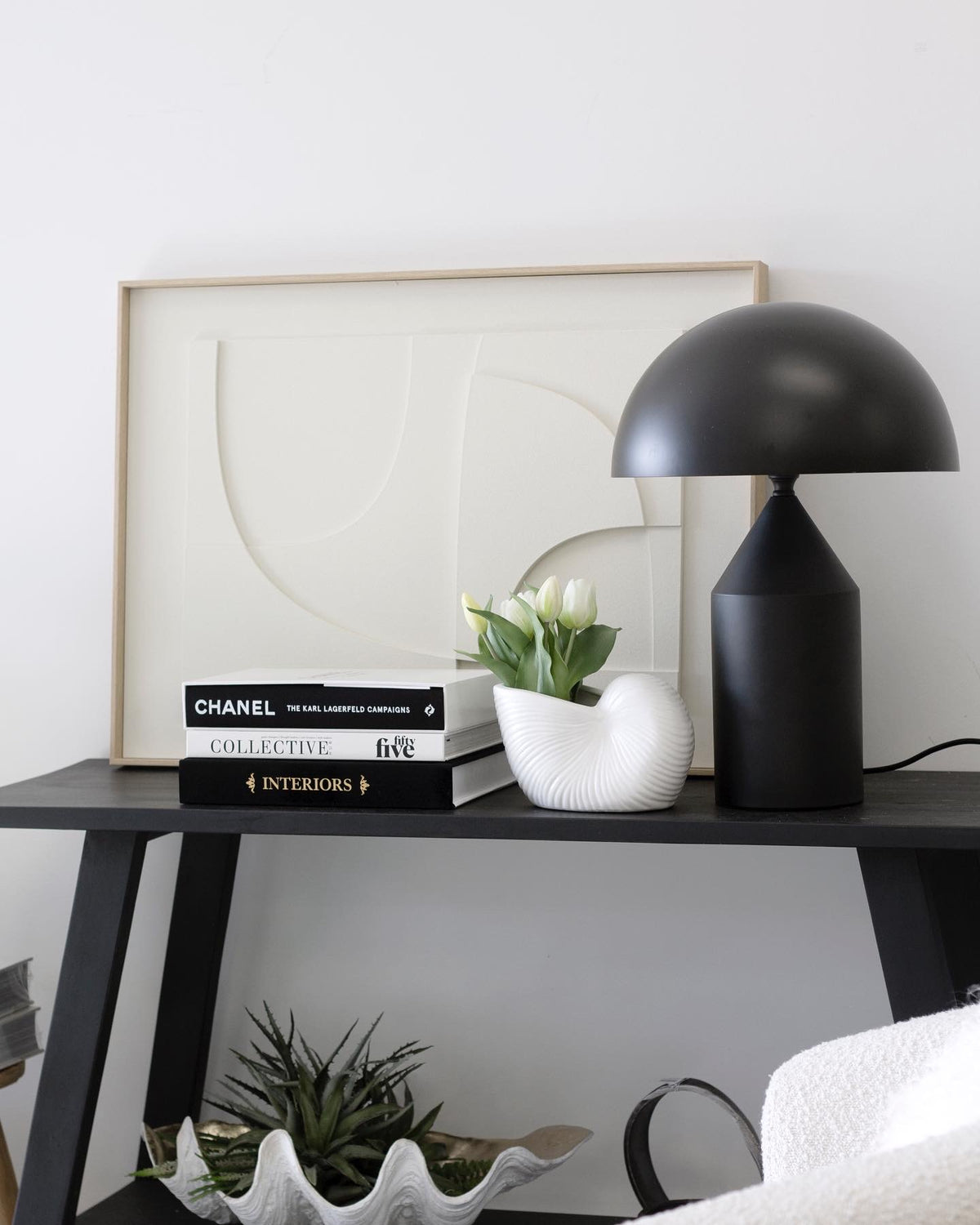 Black teak console holding a domed lamp, stacked books and a small potted plant