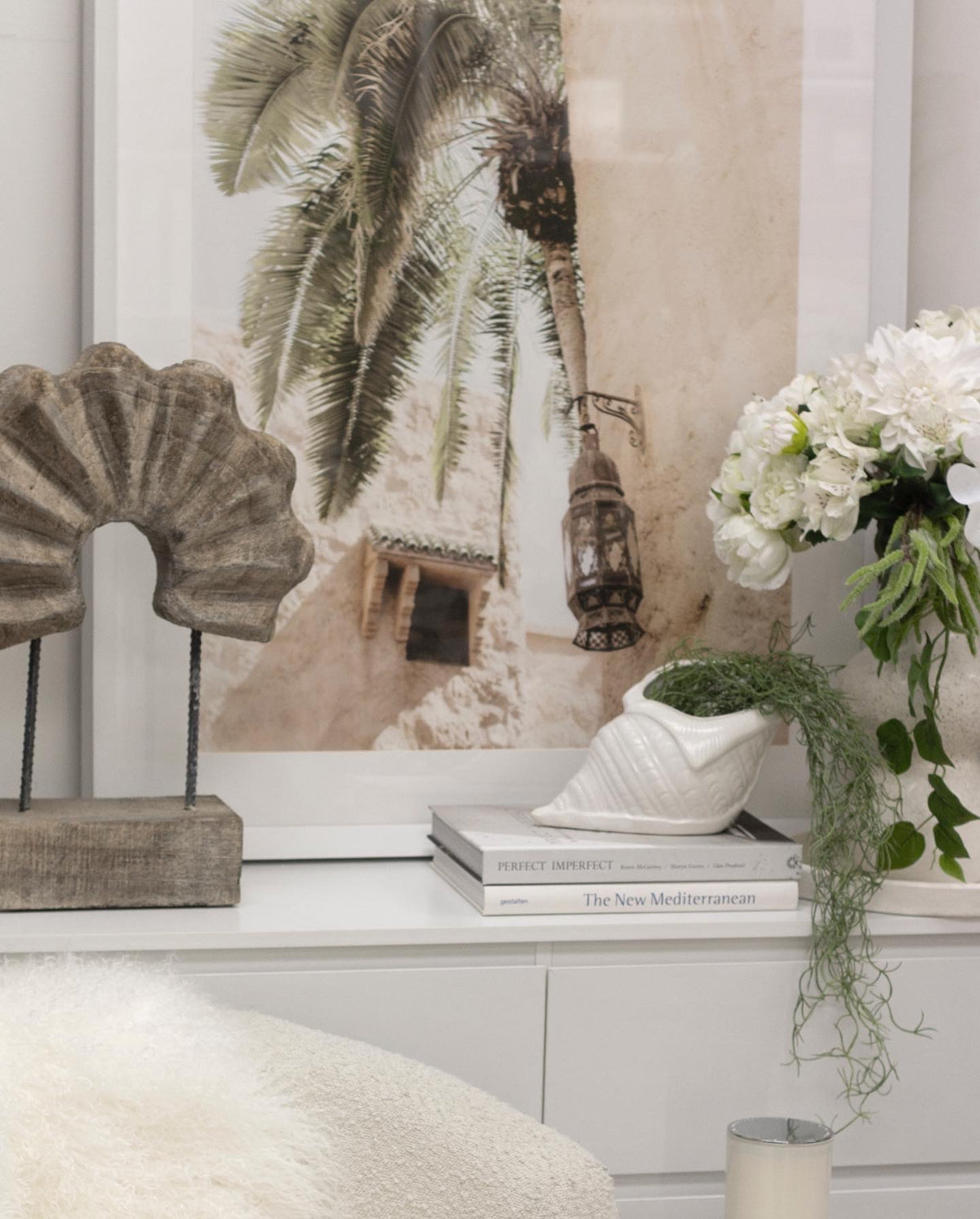 Timber arch sculpture on a sideboard in front of a large framed artwork, with white hydrangeas
