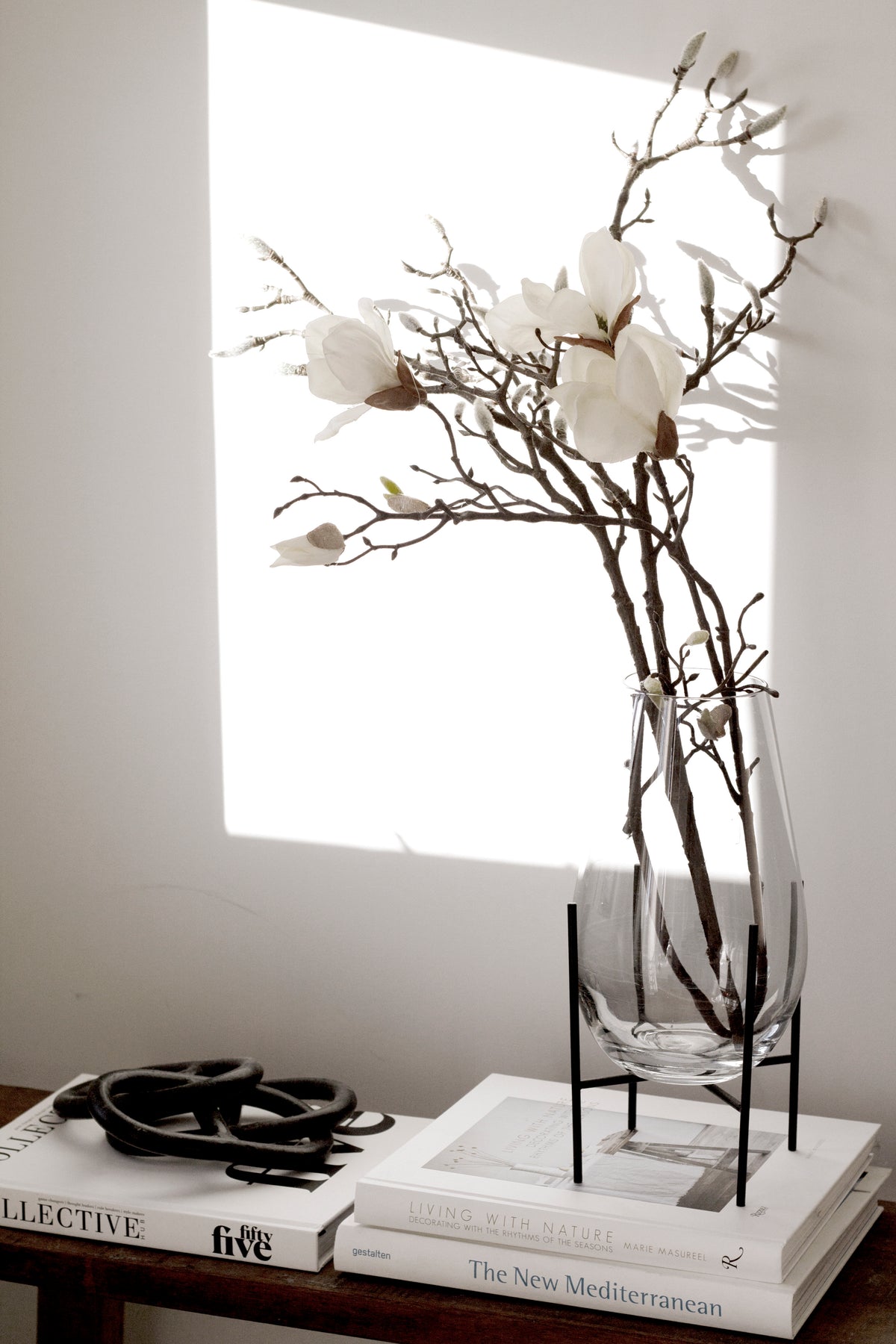 Magnolia stems in a glass vase on stacked books, with the black iron chain links on the bench alongside
