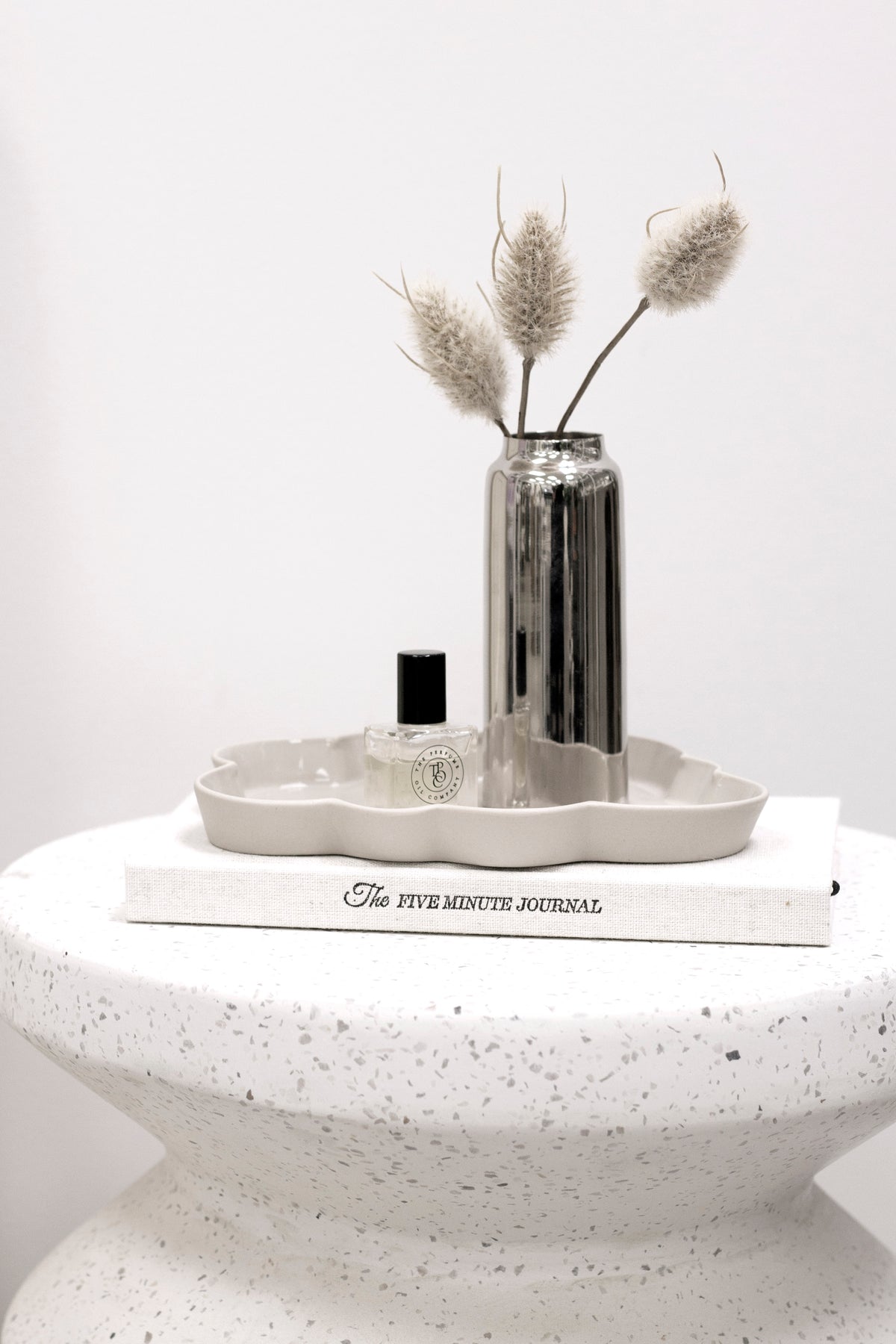 Nara stool in white speckled stone topped with a tray, silver vase and a book