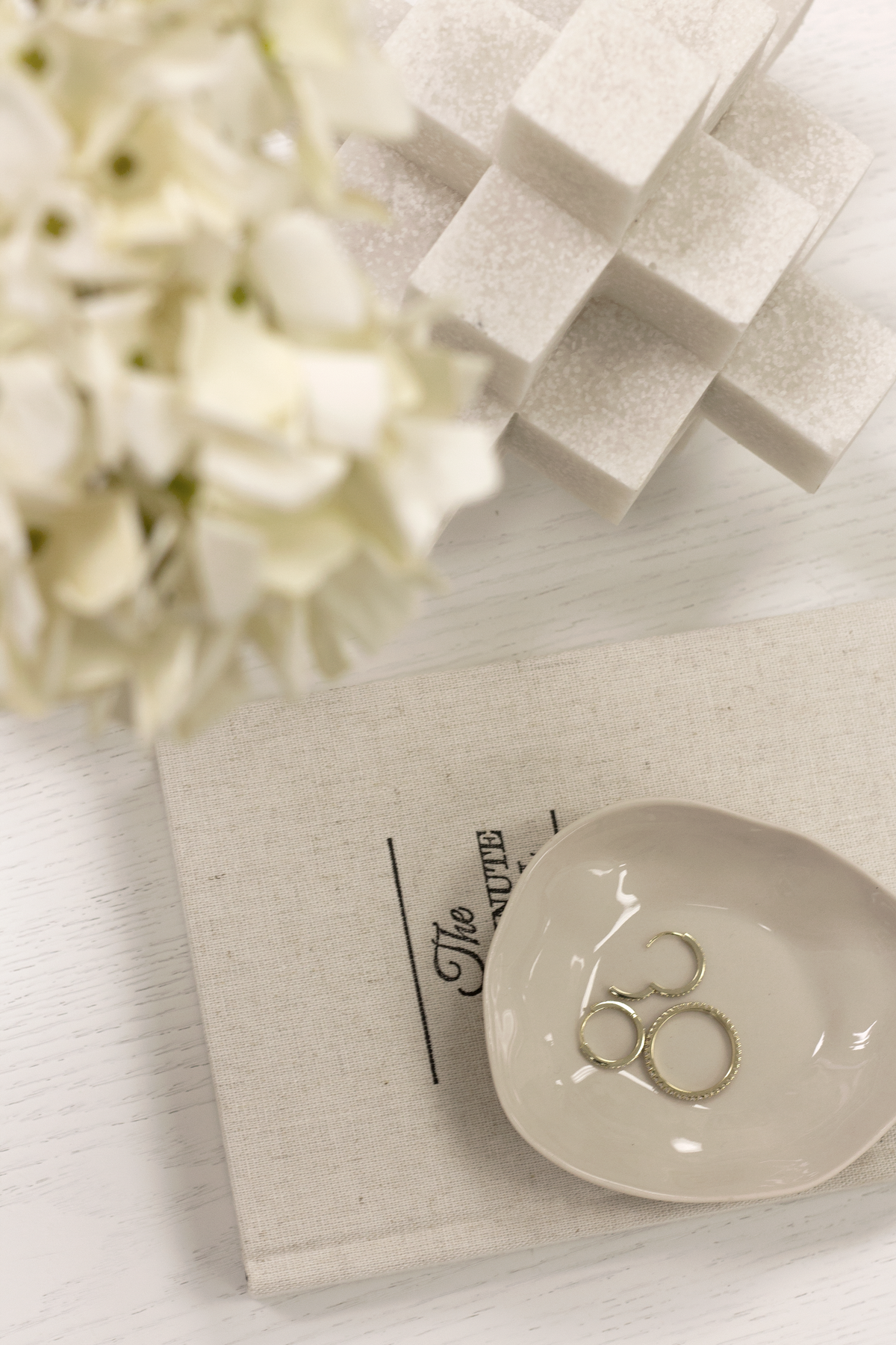 White Cubism sculpture on linen beside a dish of rings and white hydrangea