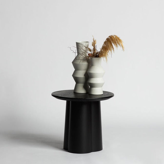 Black Strato Side Table holding a sculptural twin vase with dried grasses