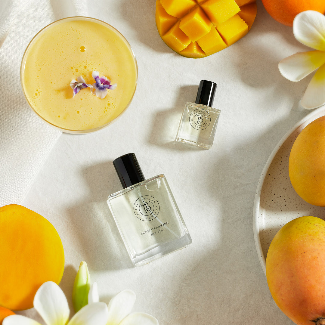 Perfume bottles on a white surface among mango, citrus slices and a cocktail