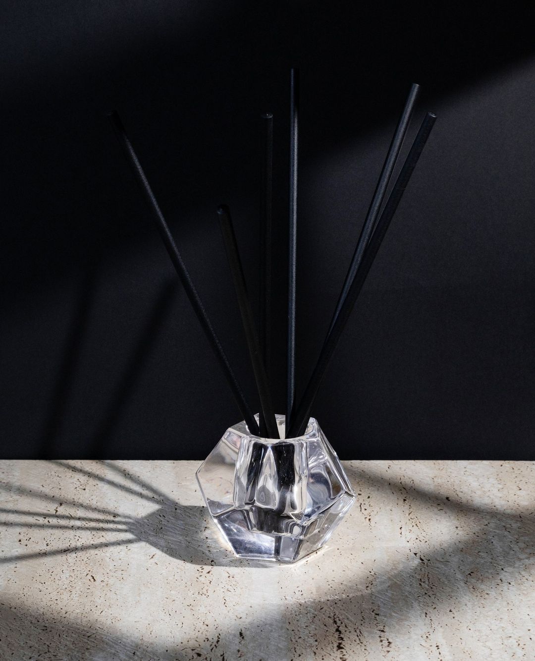 Faceted glass holder of black aroma sticks casting a long shadow on stone