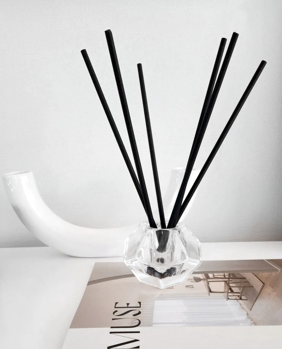 Aroma sticks in a faceted glass holder on a book beside a curved white sculpture