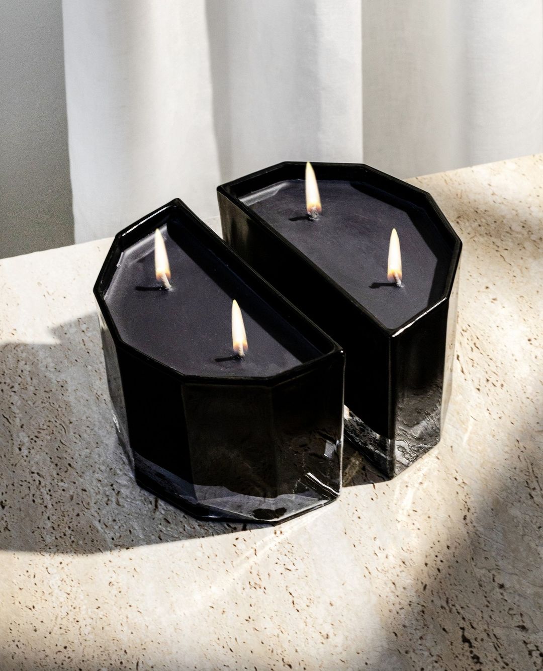 Two lit Blend candles pushed together on a sunlit travertine surface