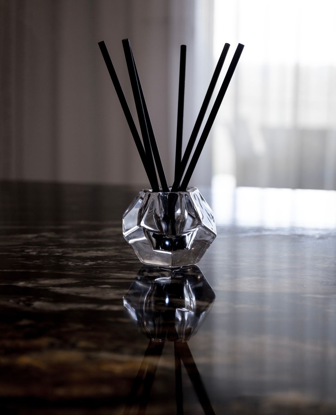 Faceted glass aroma stick holder reflected on a dark polished stone surface