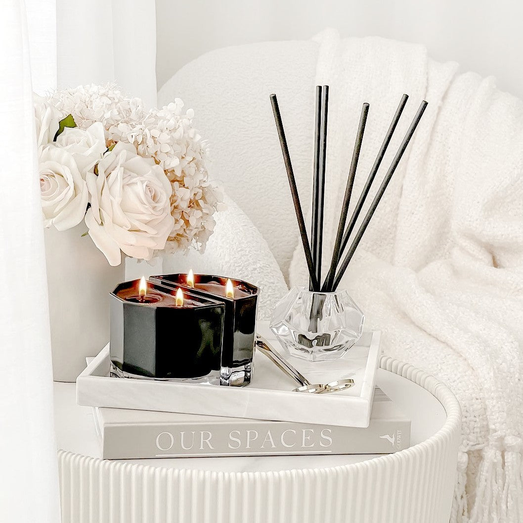 Aroma stick holder, lit Blend candle pair and white roses on a white side table stack, landscape view