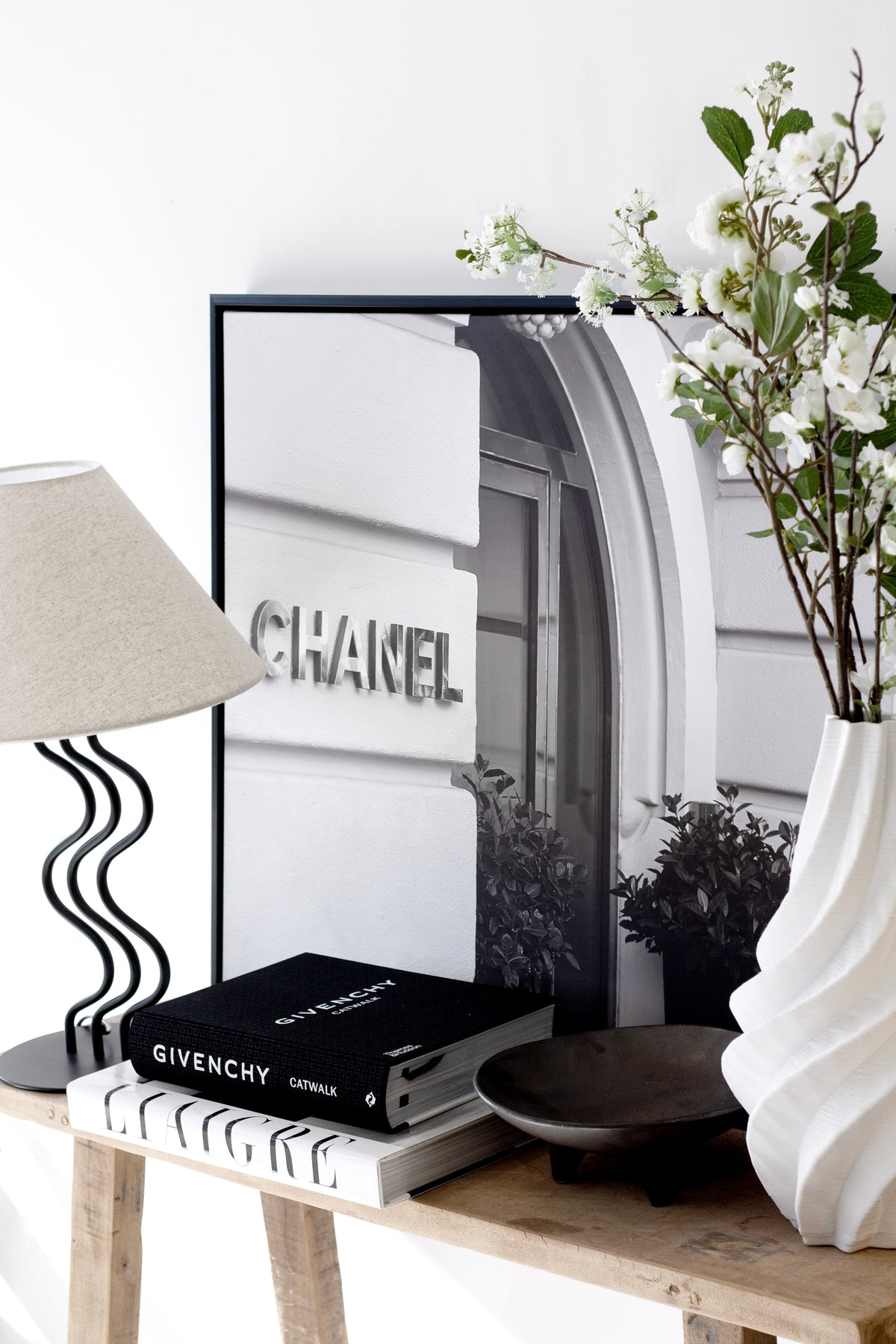 Console styled with a lamp, framed print and books beside the spiral vase of blossoms